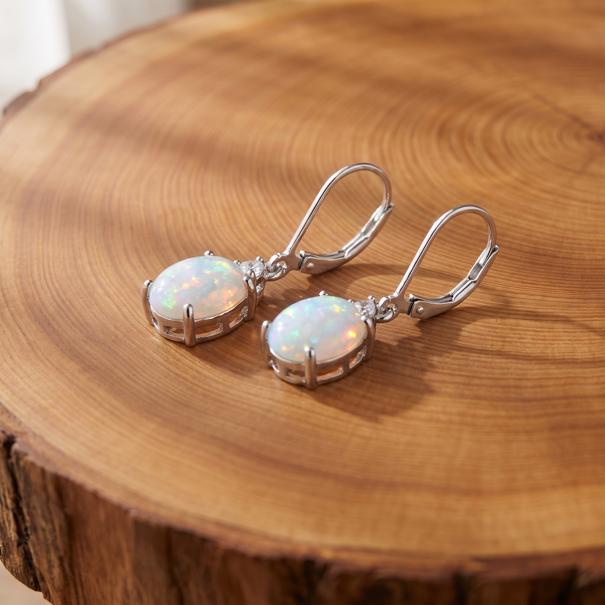 Silver oval fire opal lever-back drop earrings on a tree trunk slab